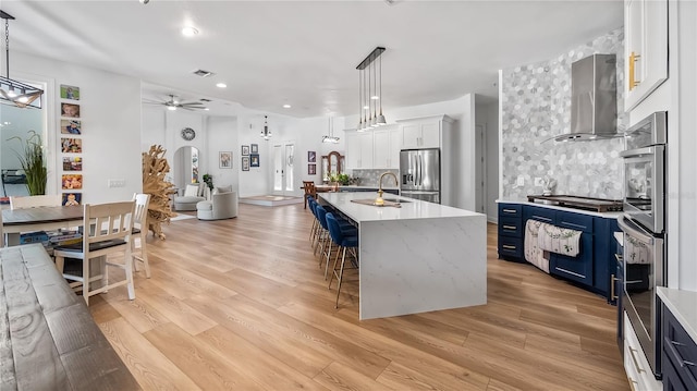 kitchen with island range hood, blue cabinetry, decorative backsplash, stainless steel appliances, and a ceiling fan