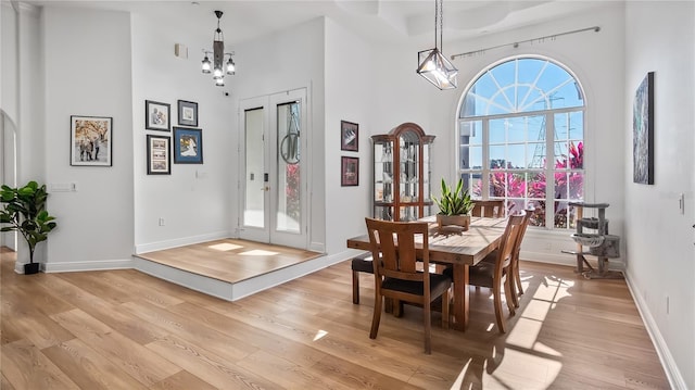 dining area with baseboards, an inviting chandelier, light wood finished floors, and a towering ceiling