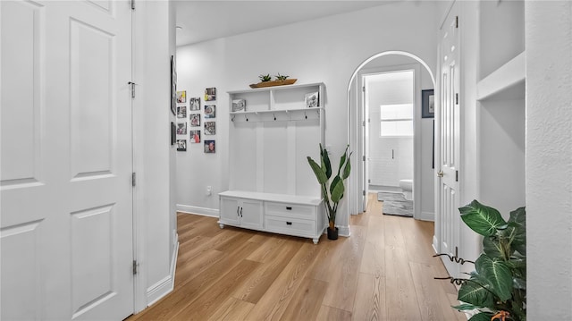 mudroom with arched walkways, baseboards, and light wood-style floors