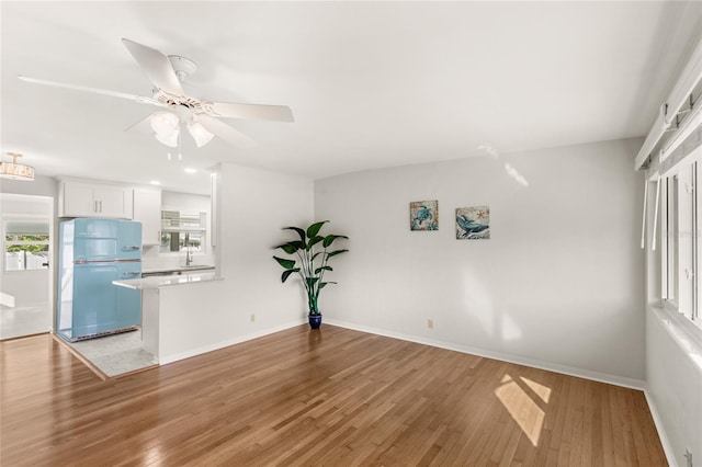 interior space featuring a sink, light wood-style flooring, baseboards, and ceiling fan