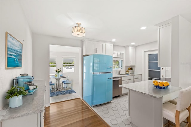 kitchen with light countertops, stainless steel dishwasher, freestanding refrigerator, white cabinets, and a sink