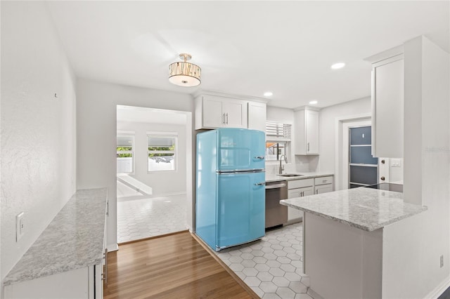 kitchen with a sink, white cabinetry, light wood-type flooring, freestanding refrigerator, and dishwasher