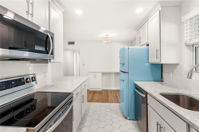 kitchen featuring stainless steel appliances, a sink, visible vents, white cabinets, and decorative backsplash