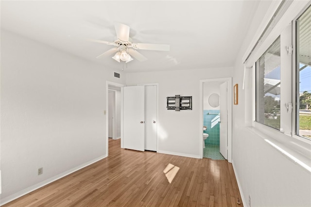 unfurnished bedroom featuring visible vents, ensuite bathroom, ceiling fan, wood finished floors, and baseboards