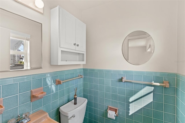 half bath featuring wainscoting, a sink, toilet, and tile walls