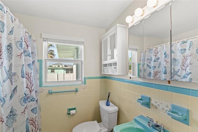 full bath with curtained shower, toilet, a sink, tile walls, and wainscoting