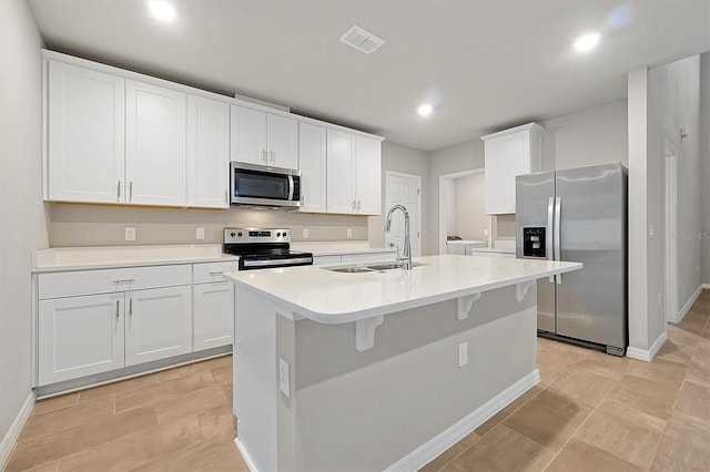 kitchen with visible vents, an island with sink, appliances with stainless steel finishes, white cabinetry, and a sink