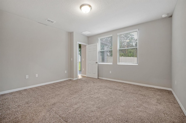 empty room featuring a textured ceiling, baseboards, visible vents, and light colored carpet