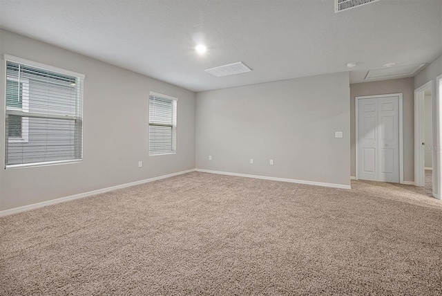 unfurnished room with a textured ceiling, carpet, visible vents, and baseboards