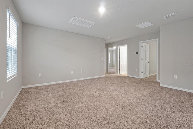 spare room featuring a wealth of natural light, visible vents, and light colored carpet