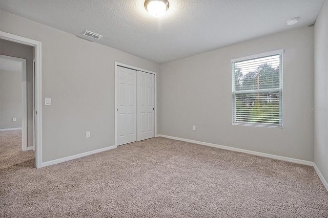 unfurnished bedroom featuring baseboards, visible vents, carpet, a textured ceiling, and a closet