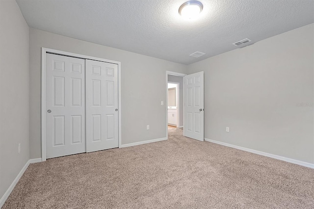 unfurnished bedroom with baseboards, visible vents, a textured ceiling, carpet floors, and a closet