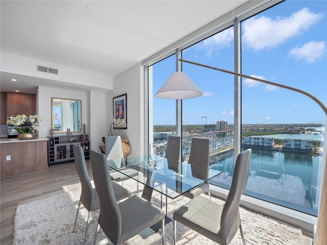 dining space featuring visible vents, light wood finished floors, a water view, and expansive windows