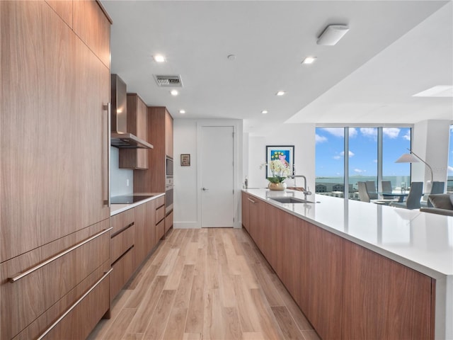 kitchen featuring a sink, modern cabinets, wall chimney exhaust hood, and light wood finished floors