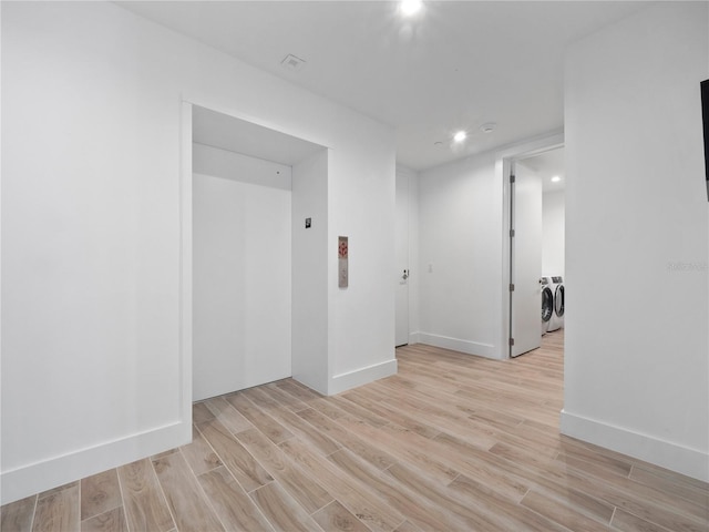 unfurnished room featuring elevator, washing machine and dryer, baseboards, and light wood-style floors