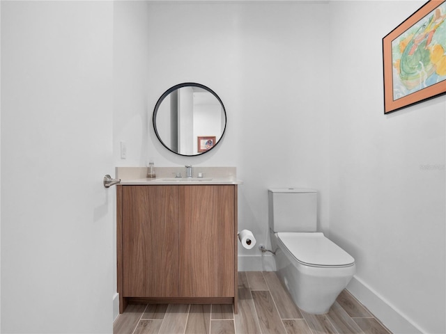 half bathroom with vanity, toilet, baseboards, and wood finish floors