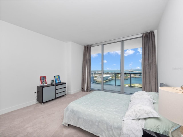 bedroom featuring a water view, light carpet, access to outside, expansive windows, and baseboards