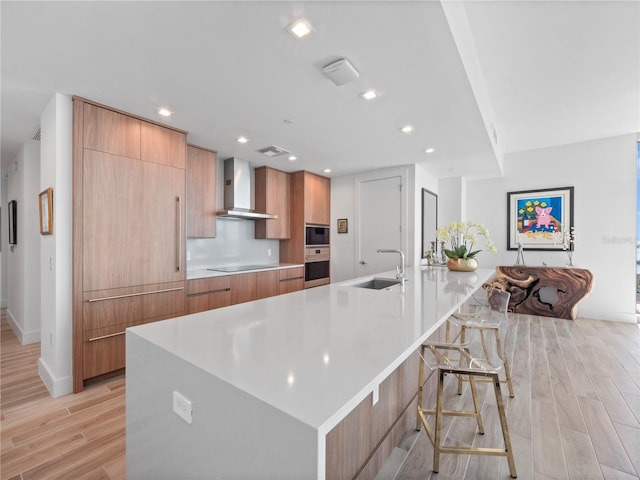 kitchen featuring modern cabinets, light wood-style flooring, a sink, recessed lighting, and wall chimney exhaust hood