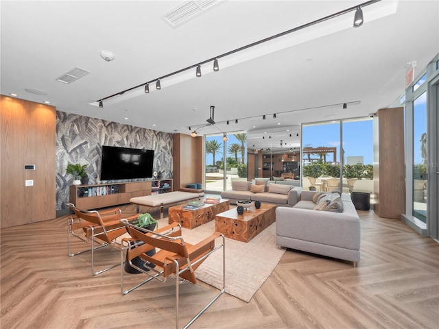 living area with visible vents, an accent wall, floor to ceiling windows, and track lighting