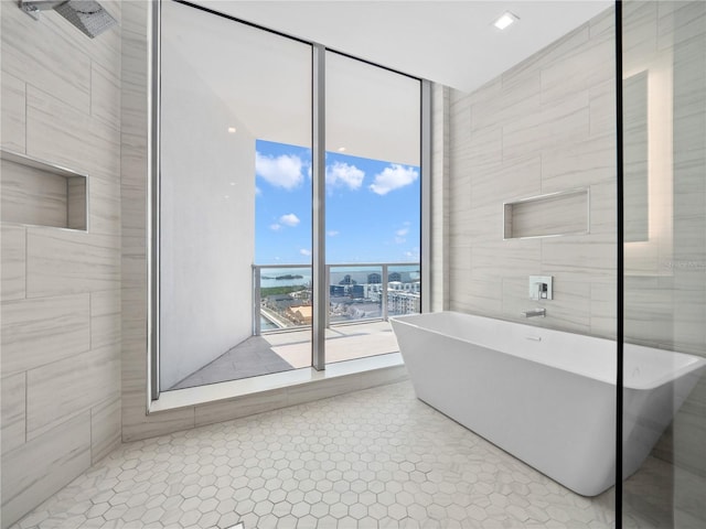 bathroom with tile patterned flooring, a soaking tub, floor to ceiling windows, and tile walls