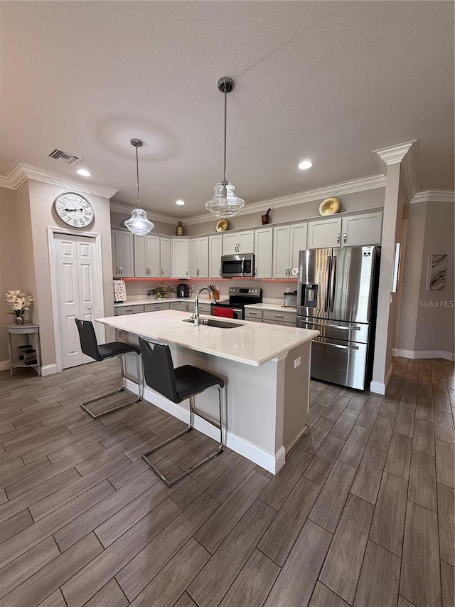 kitchen featuring visible vents, wood tiled floor, stainless steel appliances, light countertops, and a sink