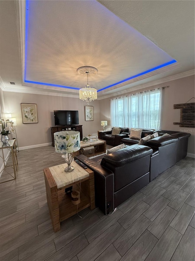 living room featuring a chandelier, baseboards, ornamental molding, wood tiled floor, and a tray ceiling