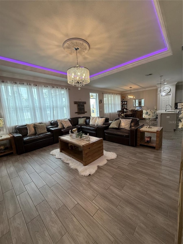 unfurnished living room with an inviting chandelier, wood tiled floor, a tray ceiling, and ornamental molding