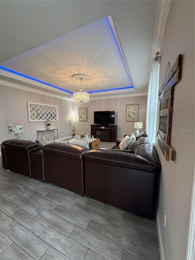 living area featuring ornamental molding, a tray ceiling, a chandelier, and baseboards