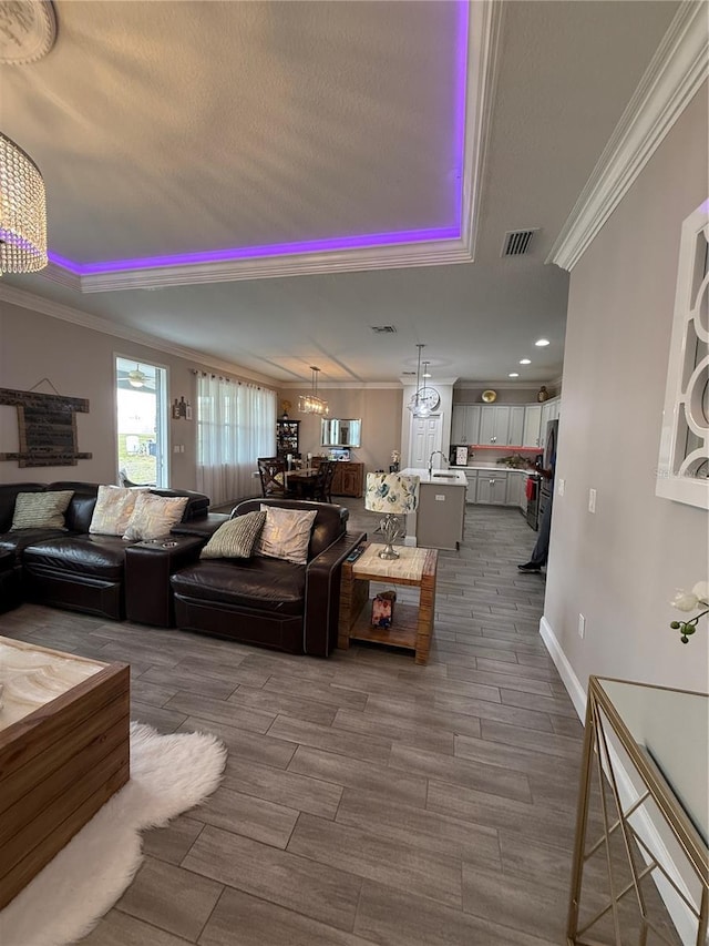 living room with crown molding, a notable chandelier, a raised ceiling, visible vents, and wood tiled floor