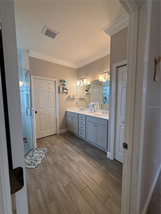 bathroom with wood finish floors, visible vents, ornamental molding, a stall shower, and a sink