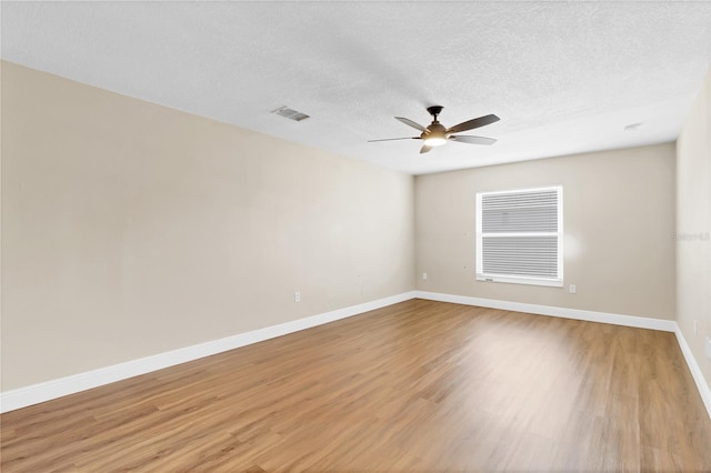 spare room with light wood-type flooring, visible vents, a textured ceiling, and baseboards