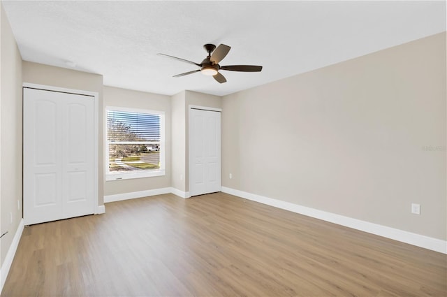 unfurnished bedroom with multiple closets, light wood-style flooring, baseboards, and a ceiling fan