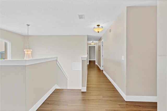 hall with light wood finished floors, visible vents, and an upstairs landing