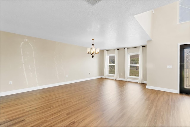 unfurnished living room with baseboards, visible vents, wood finished floors, a textured ceiling, and a notable chandelier