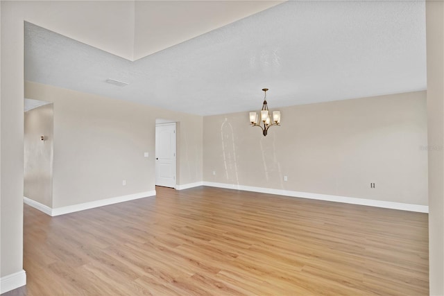 spare room featuring a chandelier, light wood-type flooring, a textured ceiling, and baseboards