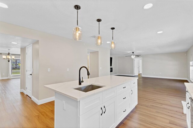 kitchen with ceiling fan with notable chandelier, a sink, light wood-style floors, open floor plan, and an island with sink