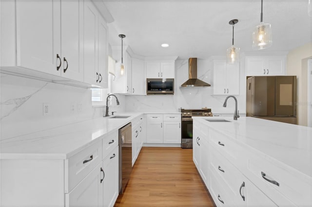 kitchen with wall chimney exhaust hood, appliances with stainless steel finishes, white cabinets, and a sink