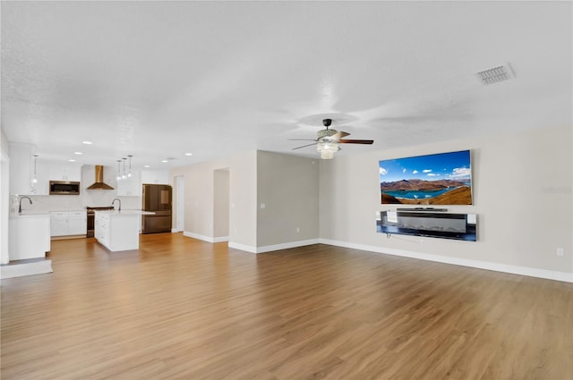 unfurnished living room featuring a ceiling fan, baseboards, visible vents, and light wood finished floors