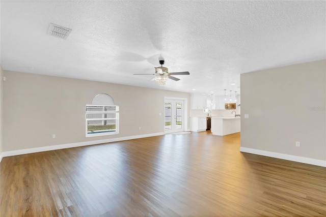 unfurnished living room featuring ceiling fan, a textured ceiling, wood finished floors, visible vents, and baseboards