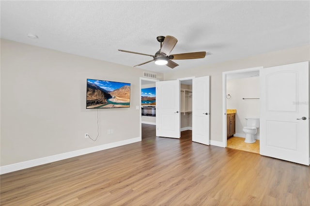 unfurnished bedroom featuring a walk in closet, visible vents, light wood-style flooring, and baseboards