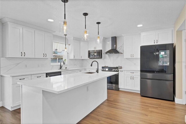 kitchen with stainless steel appliances, wall chimney range hood, a sink, and white cabinets