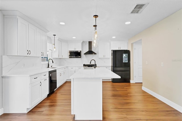 kitchen with visible vents, a kitchen island with sink, black appliances, light wood-type flooring, and wall chimney exhaust hood