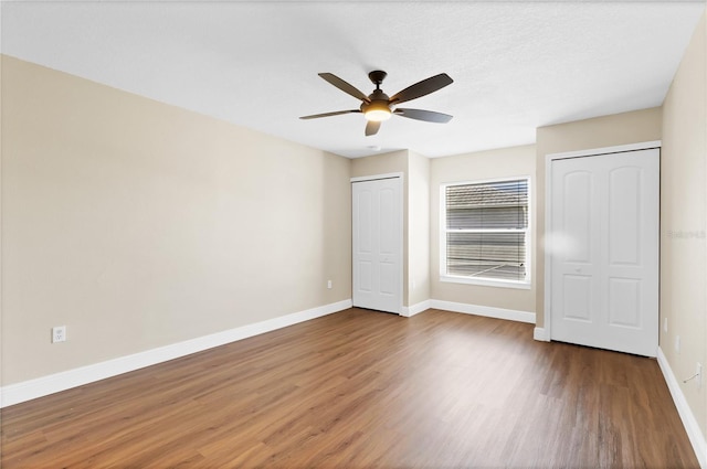 unfurnished bedroom with ceiling fan, wood finished floors, two closets, and baseboards