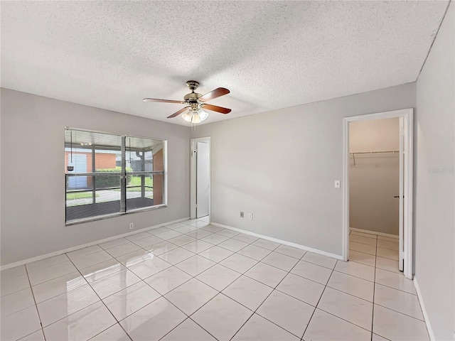 empty room with ceiling fan, baseboards, a textured ceiling, and light tile patterned flooring