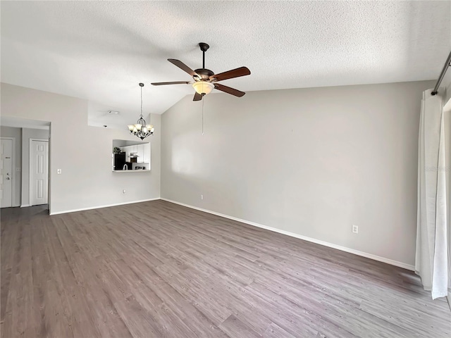 unfurnished living room with baseboards, lofted ceiling, dark wood-type flooring, a textured ceiling, and ceiling fan with notable chandelier