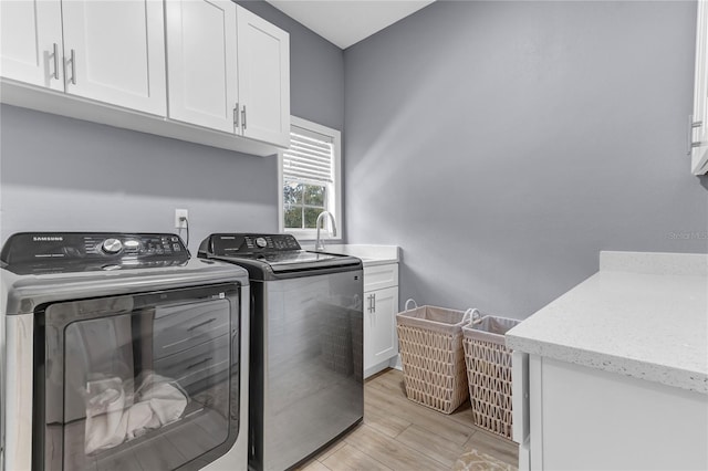 clothes washing area featuring light wood-style floors, washer and dryer, cabinet space, and a sink