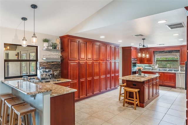 kitchen featuring visible vents, appliances with stainless steel finishes, a kitchen breakfast bar, a peninsula, and light stone countertops