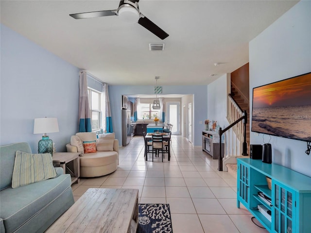 living area with a ceiling fan, visible vents, stairway, and light tile patterned floors