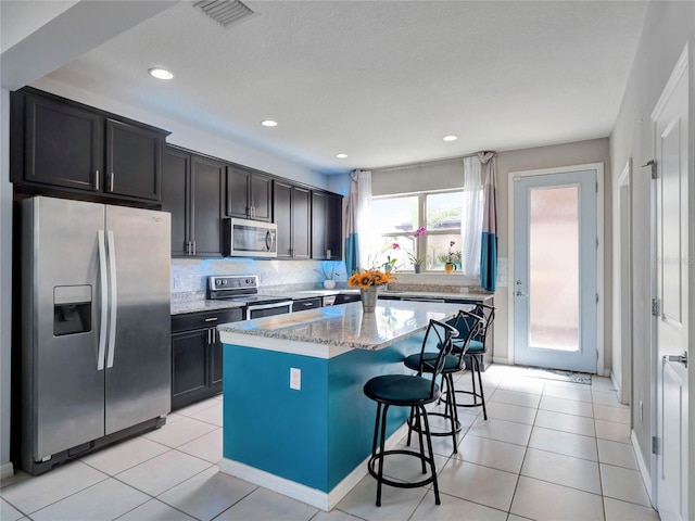 kitchen featuring light tile patterned floors, visible vents, stainless steel appliances, and a kitchen breakfast bar