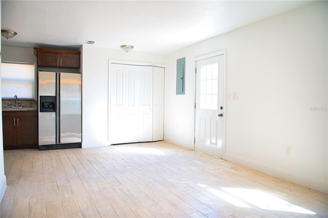 interior space with electric panel, visible vents, dark brown cabinets, light wood-style floors, and stainless steel refrigerator with ice dispenser